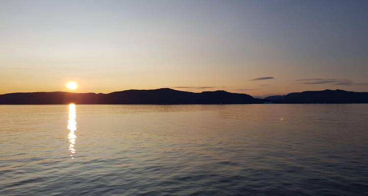 Sun setting over calm ocean waters with silhouetted shoreline.