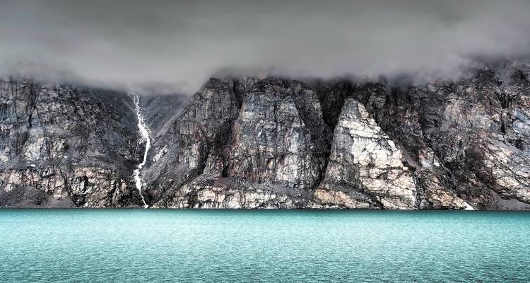 Dramatic cliffs and a waterfall meeting turquoise water.