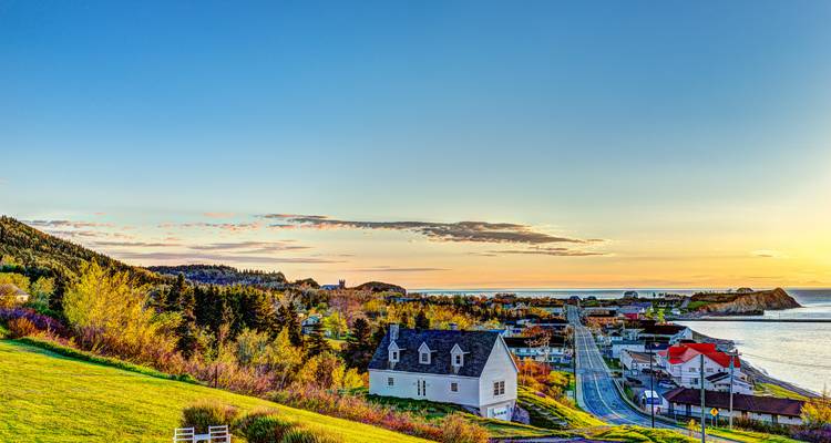 Charming coastal town at sunrise with colorful houses, church, and sea view bathed in soft light.
