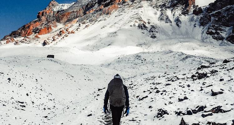 Person, die auf einem verschneiten Pfad in Richtung eines Berges mit roten Felswänden wandert.