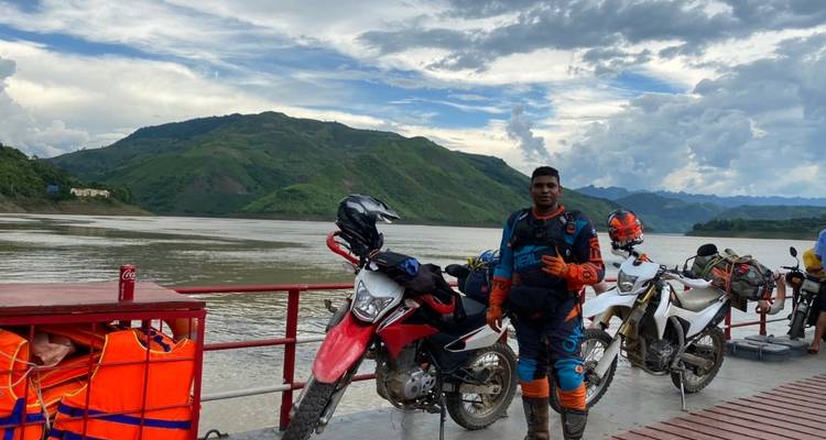 Man met motorfietsen op een veerboot die een rivier oversteekt.