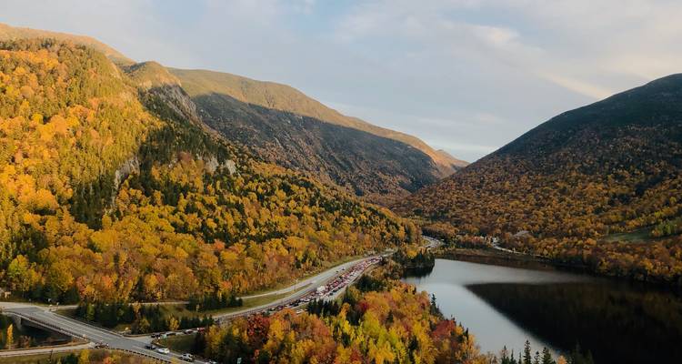 Vue panoramique d'une route et d'un lac entourés de feuillage d'automne dans une région montagneuse.