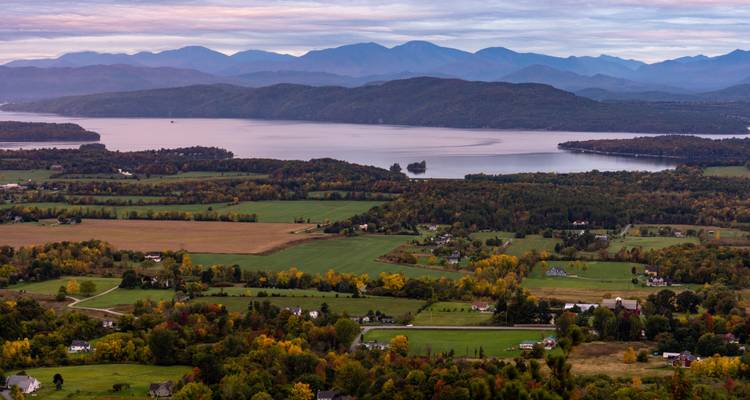 Vue panoramique d'un lac avec des champs et des montagnes au loin, mettant en valeur les couleurs d'automne.
