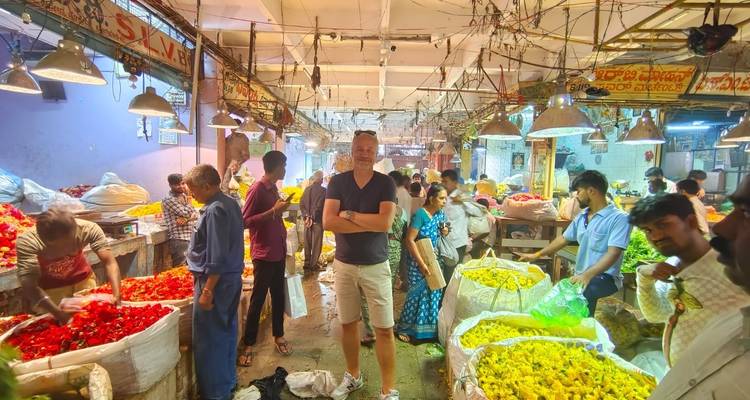Ein lebhafter überdachter Blumenmarkt mit einkaufenden Menschen und leuchtenden Farben.