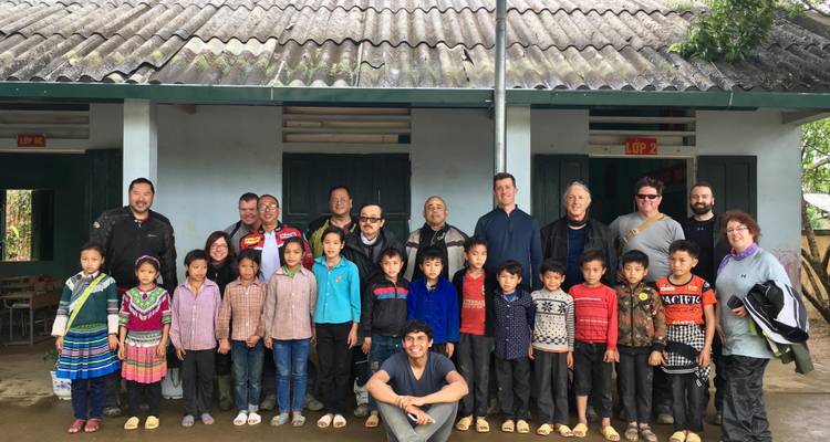 Groep poseert met kinderen voor een landelijk gebouw.