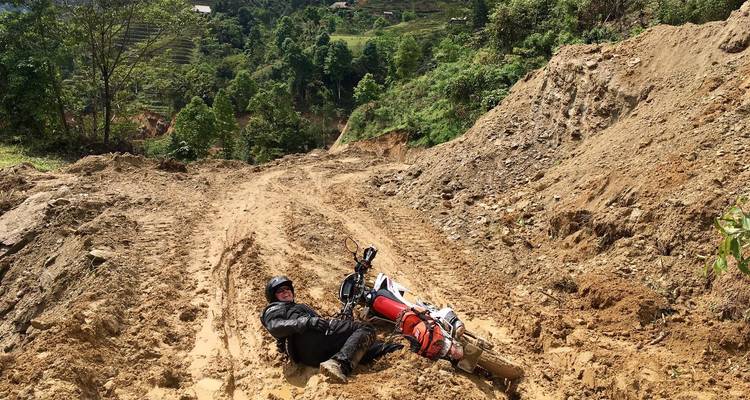 Man op de grond naast een gevallen motorfiets op een aarden heuvel.