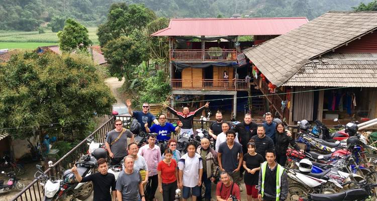 Groep mensen die poseren met motorfietsen in een landelijke omgeving.