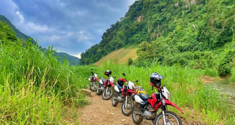 Rij rode motorfietsen geparkeerd langs een zandpad in een groene vallei.