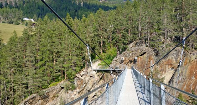 Un pont suspendu dans une zone boisée au-dessus d'un terrain rocheux.