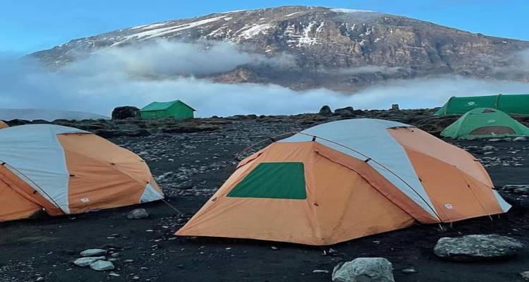 Bergcampingplatz mit orangen Zelten und einem schneebedeckten Berg im Hintergrund.