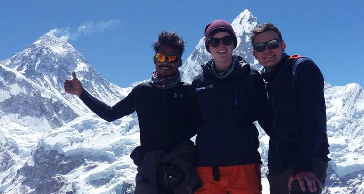 Three people posing with thumbs up in front of snowy mountains.