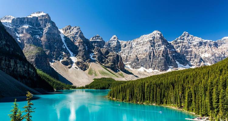 Lac glaciaire emblématique aux eaux d'un bleu éclatant, entouré de pics rocheux imposants et d'une forêt dense de conifères.