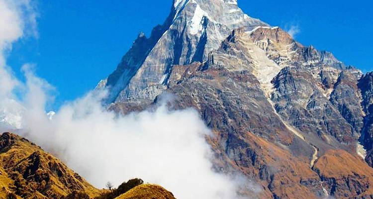 Majestätischer Berggipfel mit Wolken um seinen Fuß unter klarem Himmel.