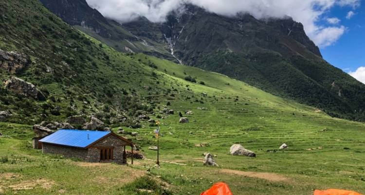Ein kleines Haus in einem grünen Tal mit Bergen im Hintergrund.
