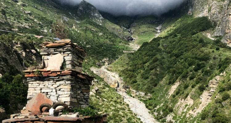 Steinstruktur in einem grünen Tal mit wolkenverhangenen Bergen.