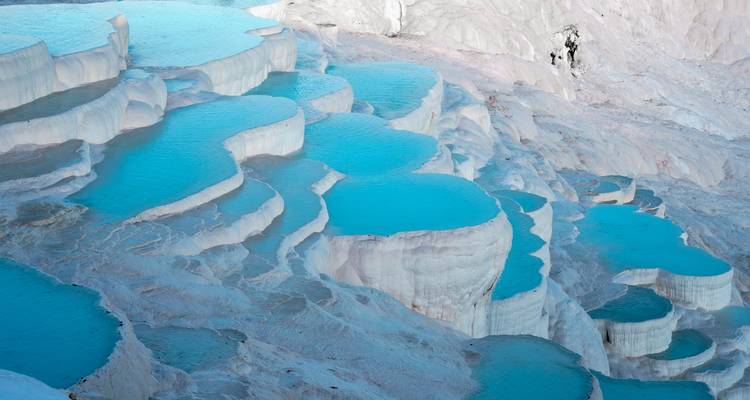 Vivid turquoise thermal pools cascading down white travertine terraces.