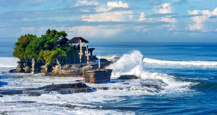 A scenic view of a temple on a rocky shoreline with crashing waves.