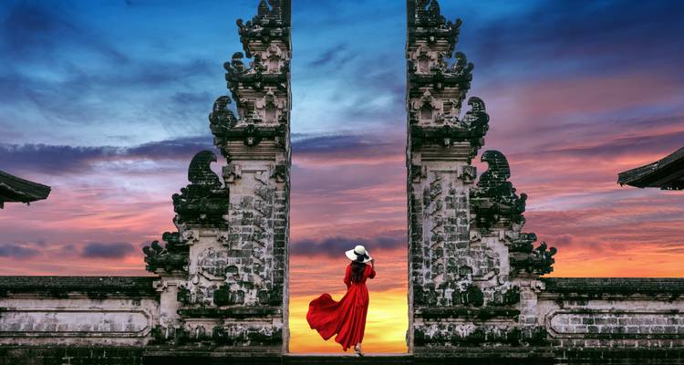 A person in a red dress standing between traditional gates during sunset.