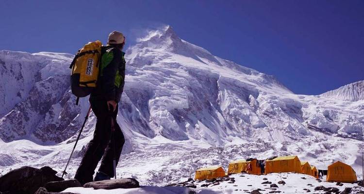 Bergsteiger steht in der Nähe eines Basislagers mit schneebedeckten Gipfeln.