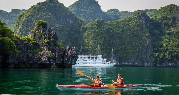 Paar beim Kajakfahren mit Kreuzfahrtschiff und Kalksteinhügeln im Hintergrund.