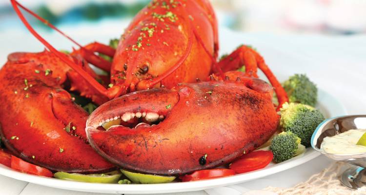 Assiette de homard bouilli d'un rouge vif garnie de citron vert, de brocoli et de tranches de tomate.