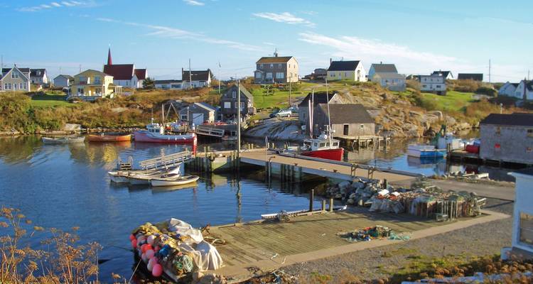 Village de pêche pittoresque avec des bateaux colorés et des chalets se reflétant dans un port calme sous un ciel bleu dégagé.