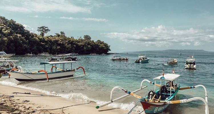 Blick auf einen Strand mit traditionellen Booten und klarem blauen Wasser.
