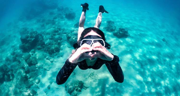 Unterwasserszene eines Schnorchlers, der mit den Händen eine Herzform bildet, inmitten von Korallenriffen.