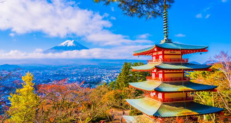 Pagoda Chureito enmarcada por el follaje de otoño con el Monte Fuji nevado elevándose por encima de las nubes en un día despejado.