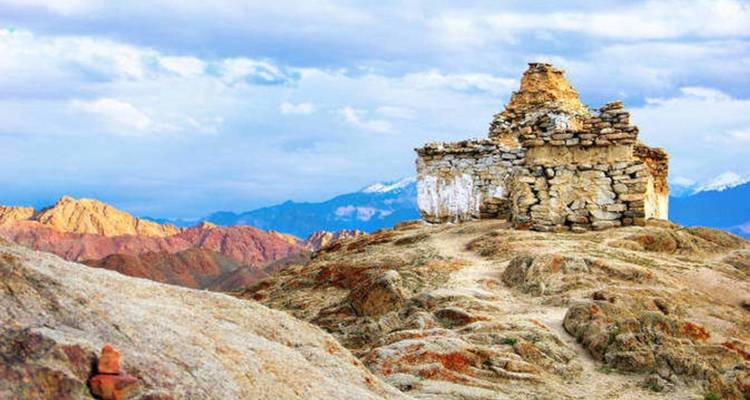 Une ancienne structure de pierre sur un sommet de colline aride avec des montagnes en arrière-plan.
