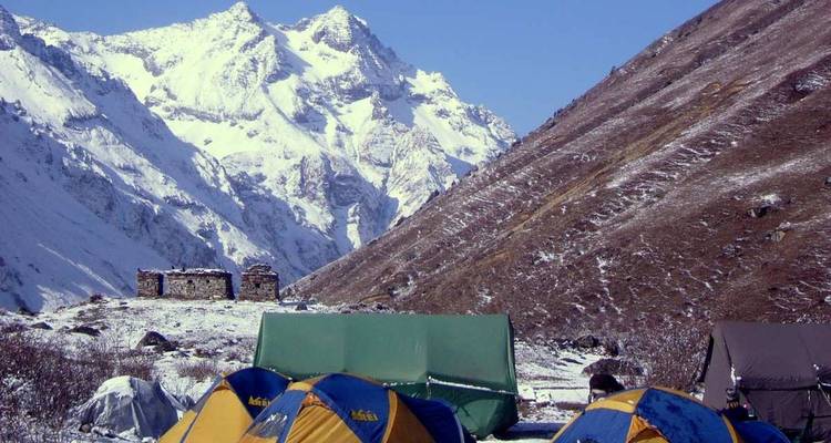 Tentes de camping installées dans une vallée de montagne enneigée.