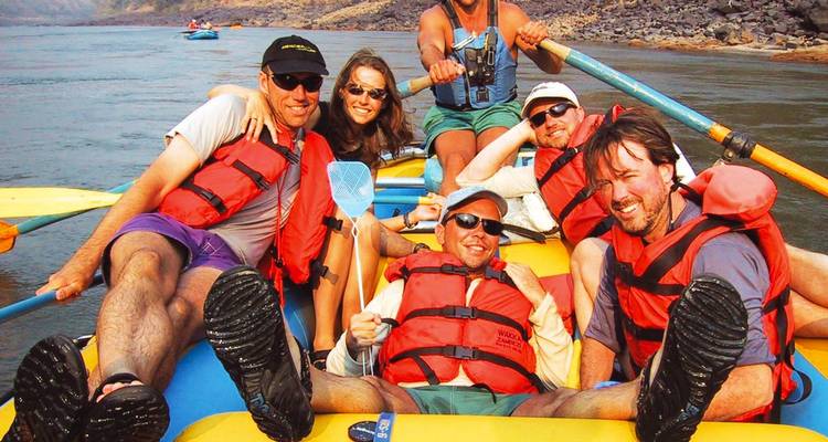 Energische Gruppe in Rettungswesten, die auf einem aufblasbaren Floß lächelt und einen Fluss hinunterpaddelt