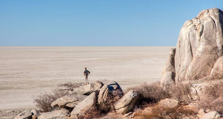 Un voyageur solitaire se tient sur un affleurement rocheux dominant l'étendue blanche et immense d'une saline.
