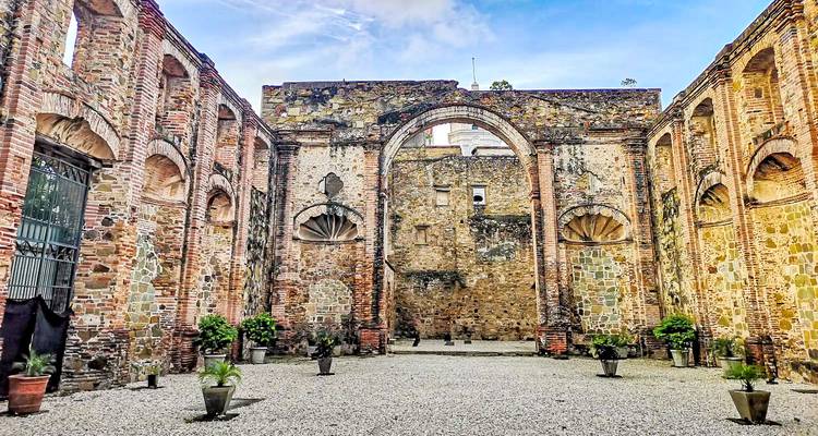 Arco de piedra antiguo y muros rodeados de plantas.