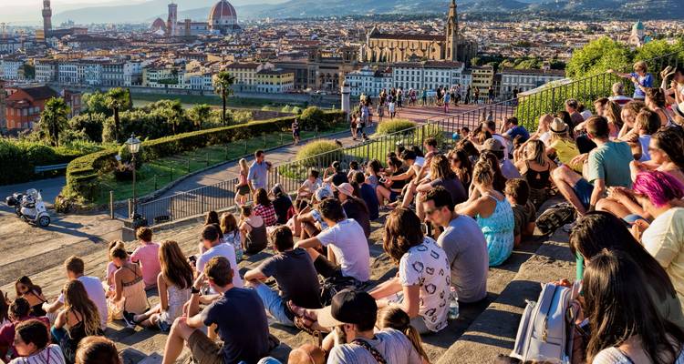 Gruppe von Menschen, die auf Stufen sitzen und auf eine Stadtlandschaft mit einer Kathedrale blicken.