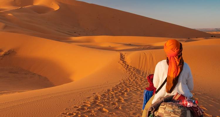 Person on camel in the desert with golden sand dunes.