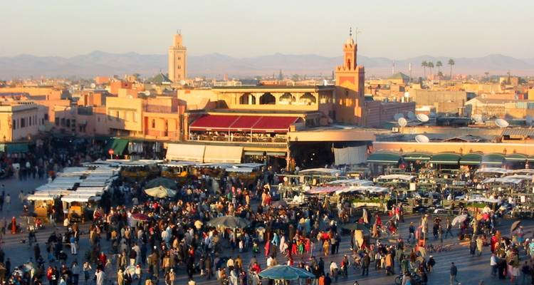 Druk marktplein in Marrakesh met traditionele architectuur.