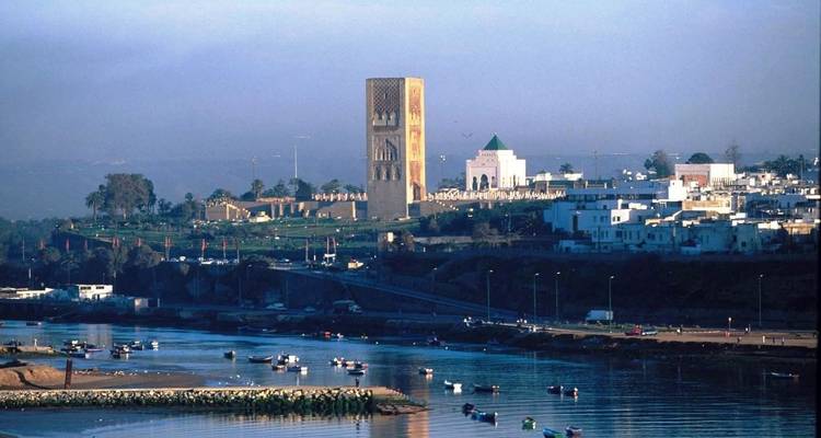 View of historical structures by a river with a city skyline in the distance.