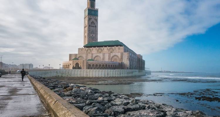 Large mosque located by the sea with overcast skies.