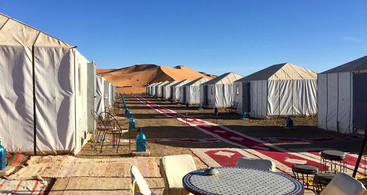 Tent camp in a desert setting with sand dunes under a blue sky.
