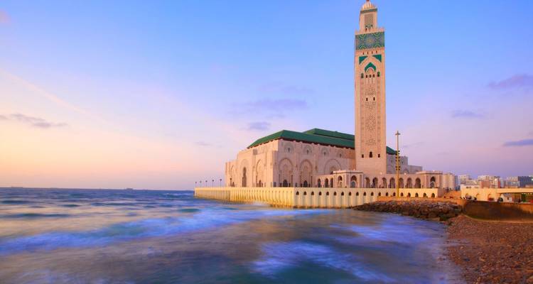 Mosque located by the sea with vibrant sunset colors in the sky.