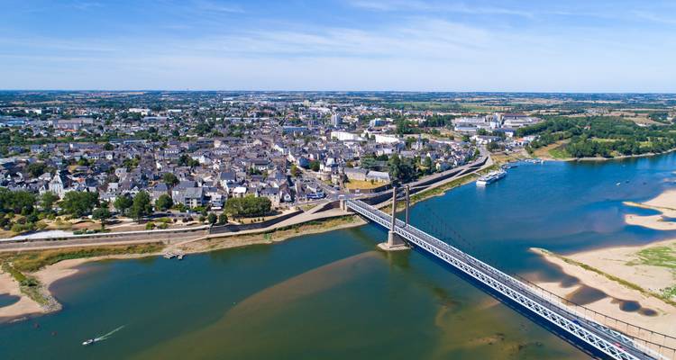 Aerial panorama of a French riverside town with suspension bridge spanning the Loire and sandy riverbanks.