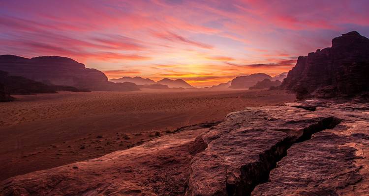 Dramatische woestijnvallei onder een levendige roze en oranje zonsonderganghemel met rotsachtige uitsteeksels