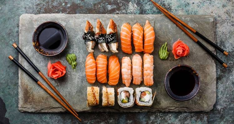 Verschiedene Sushi-Rollen ordentlich angerichtet auf einer Schieferplatte mit Zubehör.
