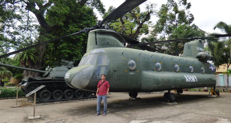 Mann posiert neben einem Militärhubschrauber und Panzer.