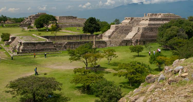 Weitläufige Aussicht auf die archäologische Stätte Monte Albán mit Terrassen und Pyramiden in einer grünen Landschaft.