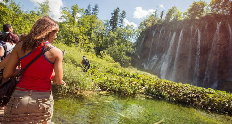Los viajeros caminan por un sendero exuberante junto a las cascadas en los Lagos de Plitvice.
