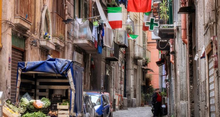 Lebendige enge Straße in Neapel mit Wäsche und italienischen Flaggen, die zwischen verwitterten Balkonen aufgehängt sind.