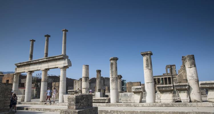 Antike Marmorsäulen und Ruinen von Pompeji unter einem klaren blauen Himmel mit Touristen, die das Gelände erkunden.