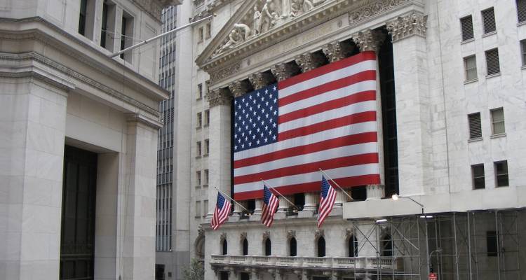 Facade of the New York Stock Exchange draped with a gigantic American flag and lined with smaller flags.